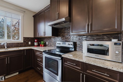 Dark wood-finish cabinetry, light-toned countertops, tile backsplash, and stainless steel appliances - 3843 Agar Green Sw, Edmonton, AB - Indoor Photo Showing Kitchen With Stainless Steel Kitchen With Upgraded Kitchen