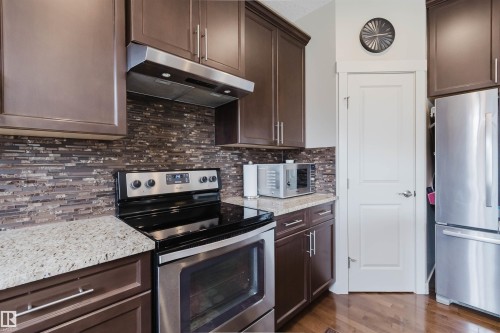 Dark wood-finish cabinetry, light-toned countertops, stainless steel appliances, and a mosaic tile backsplash - 3843 Agar Green Sw, Edmonton, AB - Indoor Photo Showing Kitchen With Stainless Steel Kitchen With Upgraded Kitchen