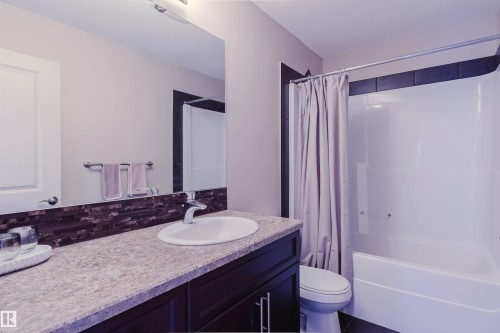 White drop-in sink with a chrome faucet, dark wood-finish vanity, and a textured backsplash - 3843 Agar Green Sw, Edmonton, AB - Indoor Photo Showing Bathroom