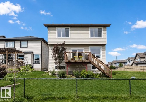 Two-story exterior with light-colored siding, a wooden deck, and a sloped grassy yard enclosed by a chain link fence - 3843 Agar Green Sw, Edmonton, AB - Outdoor