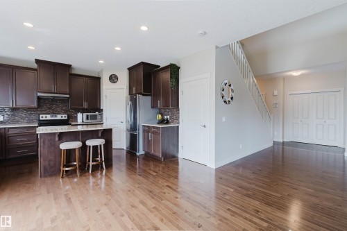 Dark wood-finish cabinetry with a tiled backsplash, a kitchen island with seating, and stainless steel appliances - 3843 Agar Green Sw, Edmonton, AB - Indoor Photo Showing Kitchen With Upgraded Kitchen
