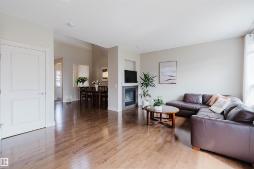 Expansive wood-finish flooring throughout, complemented by a modern fireplace with a light-toned hearth - 3843 Agar Green Sw, Edmonton, AB - Indoor Photo Showing Living Room