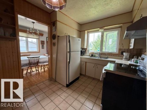 Open-concept kitchen featuring tile flooring, light-toned cabinetry, a stainless steel sink, and a large window above the sink - 13508 64 Street Nw, Edmonton, AB - Indoor Photo Showing Kitchen With Double Sink