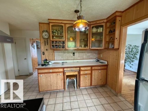 Corner kitchen counter with wood-finish cabinetry, glass-front upper cabinets, light-toned countertop, and tiled backsplash - 13508 64 Street Nw, Edmonton, AB - Indoor