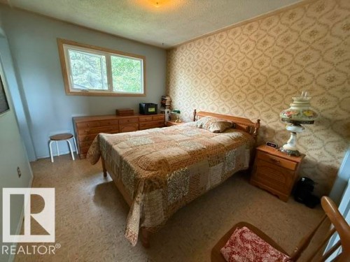 Bedroom featuring light-colored patterned wallpaper, a window with natural wood trim, wood-finish flooring, and a ceiling light fixture - 13508 64 Street Nw, Edmonton, AB - Indoor Photo Showing Bedroom