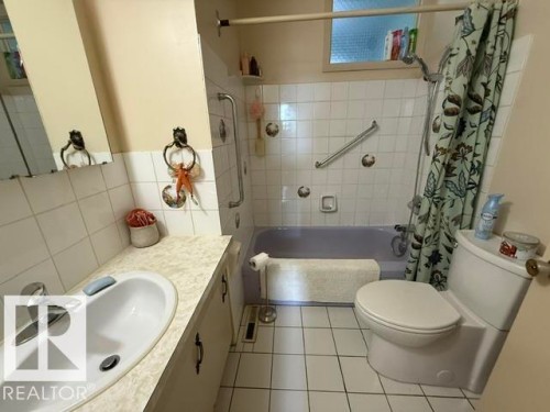 Bathroom featuring white square tile flooring and wall tiling, a built-in bathtub, a vanity with an integrated sink, and a commode - 13508 64 Street Nw, Edmonton, AB - Indoor Photo Showing Bathroom
