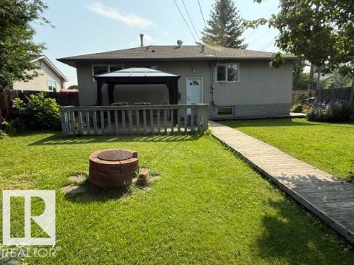 Expansive backyard featuring a manicured lawn, a wooden deck with a dark-framed gazebo, a brick fire pit, and a wooden pathway - 13508 64 Street Nw, Edmonton, AB - Outdoor