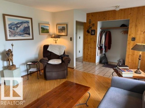 Living area featuring wood-finish flooring, white walls, and a recessed entryway with wood-paneled walls and tile flooring - 13508 64 Street Nw, Edmonton, AB - Indoor Photo Showing Living Room