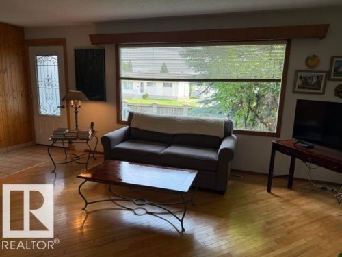 Living area featuring wood-finish flooring, a large picture window, and wood paneling - 13508 64 Street Nw, Edmonton, AB - Indoor Photo Showing Living Room