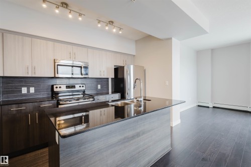 Kitchen featuring a large island with an integrated sink, stainless steel appliances, dark wood-finish flooring, and track lighting - #2207 10226 104 St Nw, Edmonton, AB - Indoor Photo Showing Kitchen With Stainless Steel Kitchen With Double Sink With Upgraded Kitchen