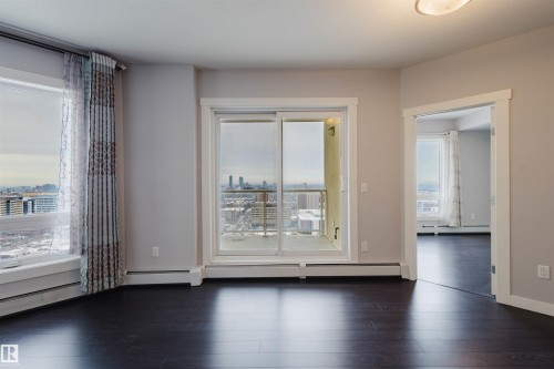 Dark wood-finish flooring, light grey painted walls, white trim throughout, large windows with city scenery, and a sliding glass door to a balcony - #2207 10226 104 St Nw, Edmonton, AB - Indoor