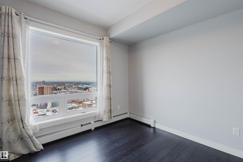 Large window framing a city skyline, dark wood-finish flooring, light grey walls, and white trim - #2207 10226 104 St Nw, Edmonton, AB - Indoor Photo Showing Other Room