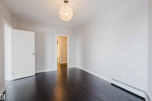 Dark wood-finish flooring with a modern pendant light fixture - #2207 10226 104 St Nw, Edmonton, AB - Indoor Photo Showing Other Room