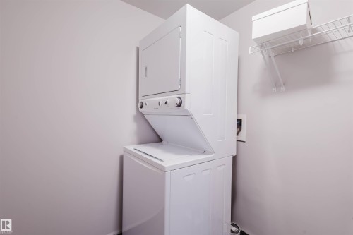 Stackable washer and dryer unit, white wire shelving, and light-toned walls - #2207 10226 104 St Nw, Edmonton, AB - Indoor Photo Showing Laundry Room