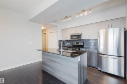 Kitchen featuring an island with a dark countertop and undermount sink, stainless steel appliances, light wood-finish cabinetry, and dark wood-finish flooring - 