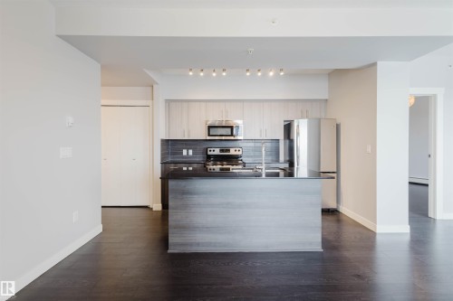 Kitchen featuring an island with a dark countertop, stainless steel appliances, light wood-finish cabinetry, and dark wood-finish flooring - #2207 10226 104 St Nw, Edmonton, AB - Indoor Photo Showing Kitchen With Stainless Steel Kitchen