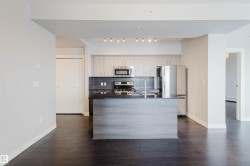 Kitchen featuring an island with a dark countertop, stainless steel appliances, light wood-finish cabinetry, and dark wood-finish flooring - 