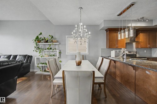 Hardwood flooring throughout, contemporary chandelier, kitchen island with stone countertop, stainless steel range hood, and wood cabinetry - 1602 Chapman Way Sw, Edmonton, AB - Indoor Photo Showing Dining Room