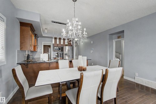 Dining area with crystal chandelier, wood-finish flooring, and a dining table with a light-toned surface - 1602 Chapman Way Sw, Edmonton, AB - Indoor Photo Showing Dining Room