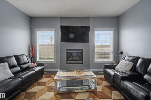Living area featuring a gas fireplace with a tiled surround, a wall-mounted display, and two windows with blinds - 1602 Chapman Way Sw, Edmonton, AB - Indoor Photo Showing Living Room With Fireplace