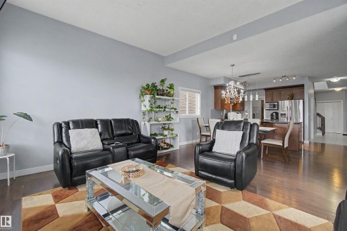 Open-concept living area with dark wood-finish flooring, a built-in kitchen island, and a decorative chandelier - 1602 Chapman Way Sw, Edmonton, AB - Indoor Photo Showing Living Room