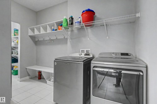 Laundry area with white tile flooring and light gray walls, featuring built-in shelving with integrated hooks and a storage bench - 1602 Chapman Way Sw, Edmonton, AB - Indoor Photo Showing Laundry Room