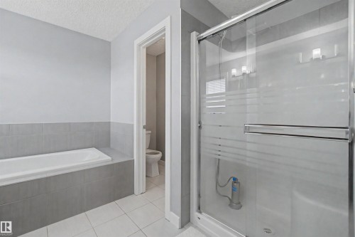 Built-in tub with gray tile surround, separate shower with sliding glass door, and a white tile floor - 1602 Chapman Way Sw, Edmonton, AB - Indoor Photo Showing Bathroom