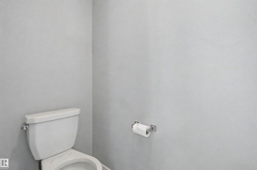 White porcelain toilet with a chrome flush lever and a wall-mounted toilet paper holder - 1602 Chapman Way Sw, Edmonton, AB - Indoor Photo Showing Bathroom