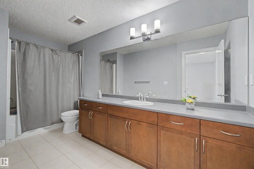Full-width vanity mirror, wood-finish cabinetry, integrated sink, and tile flooring - 1602 Chapman Way Sw, Edmonton, AB - Indoor Photo Showing Bathroom