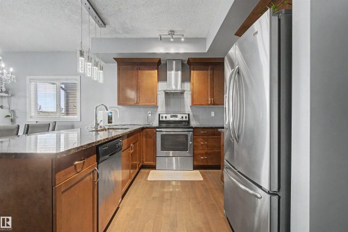 Kitchen featuring wood-finish cabinetry, stainless steel appliances, dark countertops, and wood-finish flooring - 1602 Chapman Way Sw, Edmonton, AB - Indoor Photo Showing Kitchen With Upgraded Kitchen