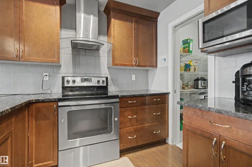 Dark wood-finish cabinetry with silver hardware, stainless steel range, built-in microwave, dark countertops, and light tile backsplash - 1602 Chapman Way Sw, Edmonton, AB - Indoor Photo Showing Kitchen
