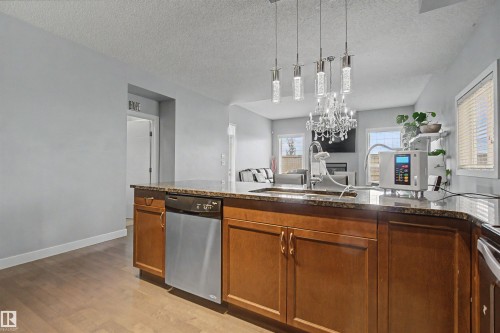 Kitchen island featuring wood cabinetry, stainless steel dishwasher, and a stone countertop with an integrated sink - 1602 Chapman Way Sw, Edmonton, AB - Indoor Photo Showing Kitchen