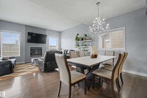 Wood-finish flooring throughout, a modern fireplace with a wall-mounted television, and a decorative chandelier above the dining area - 1602 Chapman Way Sw, Edmonton, AB - Indoor Photo Showing Dining Room With Fireplace