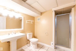 Bathroom featuring a pedestal sink with chrome fixtures, a mirrored vanity, a commode, a shower stall with a frosted glass door, and a tiled floor - 