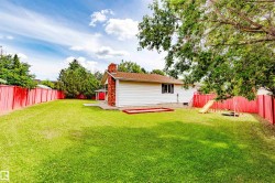 Expansive rear yard featuring a vibrant red privacy fence, mature trees, and a brick chimney exterior accent - 