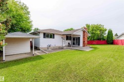 Expansive rear yard featuring a large patio, white siding, and a red brick chimney - 
