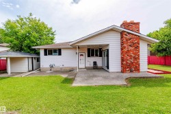 Expansive backyard featuring a manicured lawn, an exposed aggregate patio, a prominent brick chimney, and a detached carport with an enclosed storage shed - 