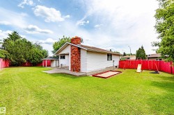 Spacious backyard featuring a large green lawn, concrete patio, and a red-painted privacy fence - 