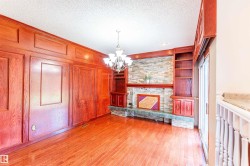 Room featuring wood-finish flooring, wood paneling, and a stone-faced fireplace with a stone hearth - 