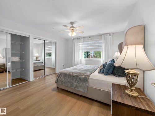 Wood-finish flooring, mirrored sliding closet doors with built-in shelving, window with blinds and sheer curtains, and a ceiling fan. - #314 237 Youville Dr E Nw, Edmonton, AB - Indoor Photo Showing Bedroom