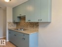 Custom-colored cabinetry with modern hardware, mosaic tile backsplash, double basin stainless steel sink, and wood-finish flooring - #31 11255 31 Av Nw, Edmonton, AB  - Indoor Photo Showing Kitchen With Double Sink 