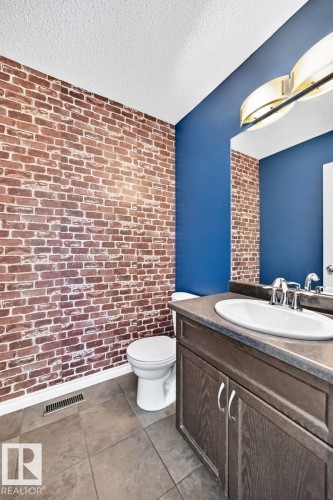 Brick-pattern accent wall, contrasting blue painted wall, recessed lighting, tile flooring, and a vanity with a white basin sink - 217 Silverstone Crescent, Stony Plain, AB - Indoor Photo Showing Bathroom
