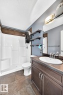 White shower surround with built-in shelving, dark wood-finish vanity with an integrated sink, and large format floor tiles - 