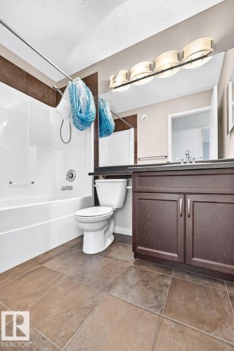 Tile flooring, deep brown vanity, white bathtub, wall-mounted mirror, and multi-bulb vanity lighting - 217 Silverstone Crescent, Stony Plain, AB - Indoor Photo Showing Bathroom
