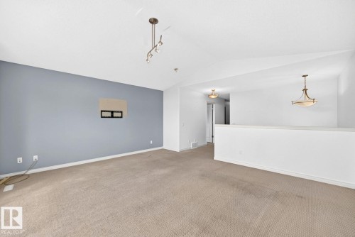 Vaulted ceiling, track lighting fixture, ceiling-mounted light fixture, carpeted flooring, and a half-wall partition - 217 Silverstone Crescent, Stony Plain, AB - Indoor Photo Showing Other Room