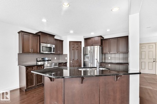Kitchen featuring a center island with a sink, dark wood-finish cabinetry, stainless steel appliances, and wood-finish flooring - 217 Silverstone Crescent, Stony Plain, AB - Indoor Photo Showing Kitchen With Double Sink With Upgraded Kitchen