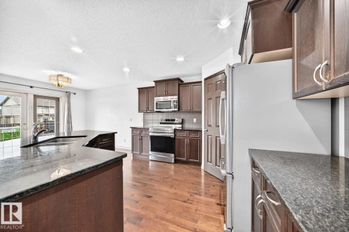 Spacious kitchen with a central island, dark wood cabinetry, stainless steel appliances, and stone-finish countertops - 217 Silverstone Crescent, Stony Plain, AB - Indoor Photo Showing Kitchen With Upgraded Kitchen