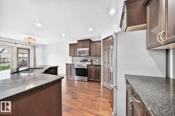 Spacious kitchen with a central island, dark wood cabinetry, stainless steel appliances, and stone-finish countertops - 