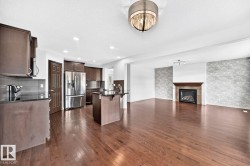 Hardwood flooring, dark wood cabinetry, stainless steel appliances, central island with seating, and a fireplace with a stone surround and wood mantel - 