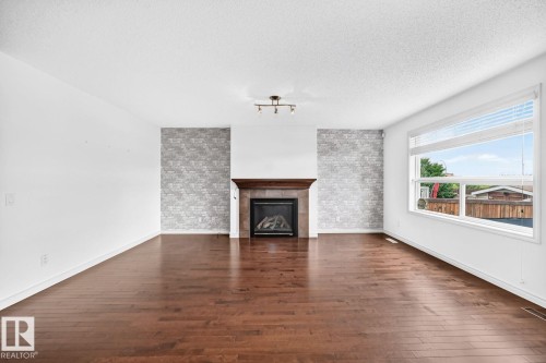 Warm wood-finish flooring complements the interior space - 217 Silverstone Crescent, Stony Plain, AB - Indoor Photo Showing Living Room With Fireplace